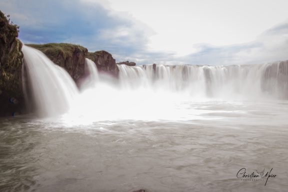 Breiter Wasserfall mit schäumendem Wasser und nebliger Umgebung.